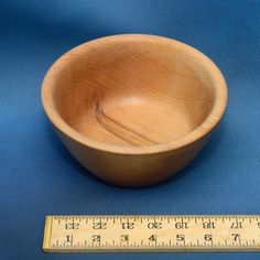 a wooden bowl sitting on top of a blue surface next to a measuring tape and ruler