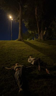 two people laying in the grass under a street light at night with their heads down