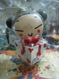 a teddy bear in a box with a heart on its chest and eyes closed, sitting on a table