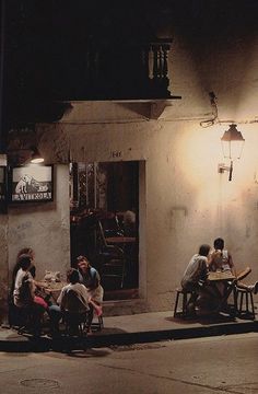 several people sitting at tables on the sidewalk in front of a building