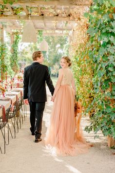 a bride and groom holding hands walking down the aisle at their outdoor wedding reception under an arbor