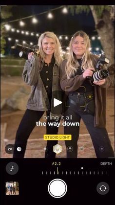 two women standing next to each other in front of a tree with lights on it