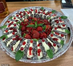 a cake decorated with strawberries, raspberries and mint leaves on a table