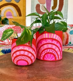 two pink vases with plants in them sitting on a table next to colorful pillows