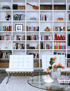 a living room filled with lots of white furniture and bookshelves full of books