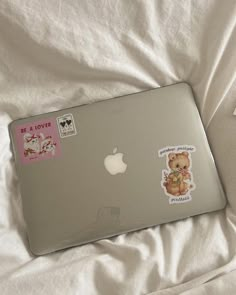 an apple laptop with stickers on it sitting on a white sheeted bed spread