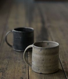 two coffee mugs sitting on top of a wooden table next to each other, one black and the other white