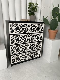 a black and white chest of drawers next to a potted cacti plant