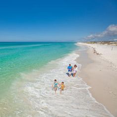 people are walking along the beach with clear water and blue skies in the background on a sunny day