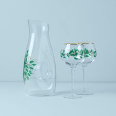 two wine glasses sitting next to each other on a white counter top, one with green leaves painted on it