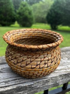 a woven basket sitting on top of a wooden table next to a park bench with trees in the background