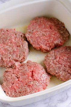 four hamburger patties in a white casserole dish on a marble counter top