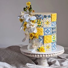 a multi - colored cake with white and yellow flowers on top sits on a pedestal