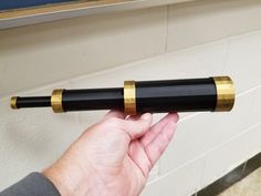 a hand holding a black and gold telescope