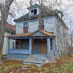 an old run down blue house in the middle of some trees and grass with no leaves on it