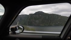 a car's side view mirror with mountains in the back ground and water behind it