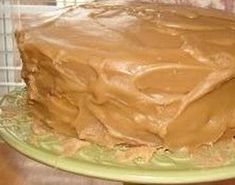 a chocolate cake with frosting sitting on top of a green plate in front of a window