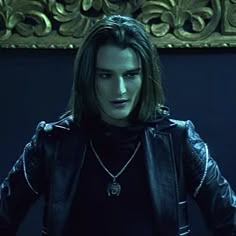 a man with long hair wearing a black leather jacket and holding his hands on his hips