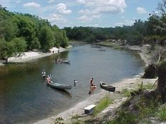 people are standing in the water near boats and canoes on the river bank,