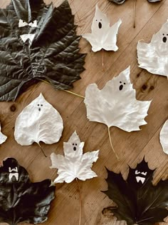 paper leaves with ghost faces on them sitting on a wooden table next to other leaf shapes