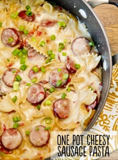 a skillet filled with pasta, sausage and cheese on top of a wooden table