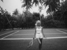 a black and white photo of a woman holding a tennis racket on a tennis court