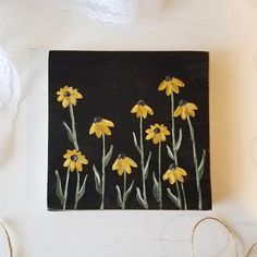 some yellow flowers are on a black and white board with twine, scissors and lace