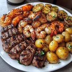 a white plate topped with steak, potatoes and shrimp