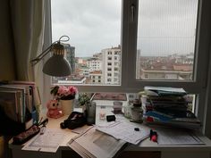 a cluttered desk in front of a large window with cityscape on it