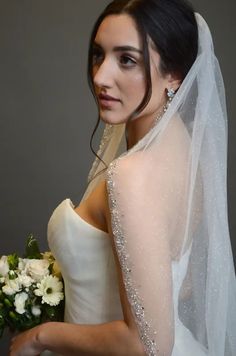 a woman in a wedding dress holding a bouquet of flowers and wearing a bridal veil