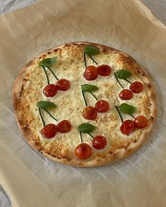 a pizza with cherry tomatoes and basil on it sitting on wax paper, ready to be eaten