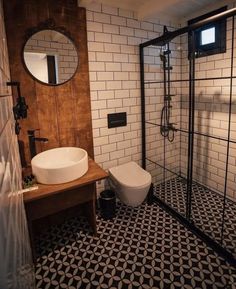 a white toilet sitting next to a walk in shower under a bathroom mirror on top of a wooden counter