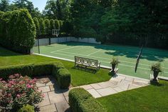 an aerial view of a tennis court surrounded by greenery and flowers, with a bench in the foreground