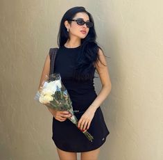 a woman in black dress holding flowers and wearing sunglasses