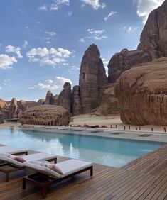 two chaise lounges sitting on the deck next to a swimming pool with mountains in the background