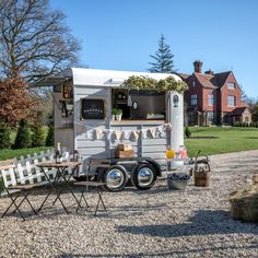 a food truck parked on gravel with chairs around it and a table in front of it