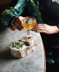 a person is holding a drink in front of a piece of food on a table