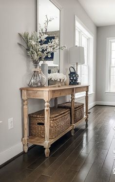 a wooden table with baskets and flowers on it in front of a large mirror above