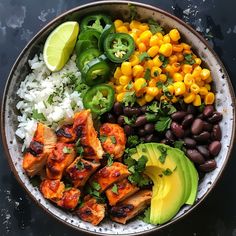 a bowl filled with rice, black beans, corn and avocado next to lime wedges