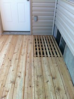 a wooden floor in front of a white door with a drain grate on it