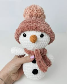 a hand holding a small crocheted snowman with a hat and scarf on