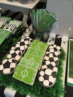 a table topped with cookies and cupcakes covered in green frosting next to soccer field decorations