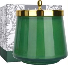 a green glass candle with a gold lid in front of a white box and an ornament