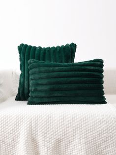 two green velvet pillows sitting on top of a white couch next to a white wall