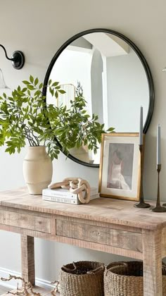 a wooden table with baskets on it and a round mirror above it, next to a potted plant