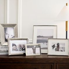 there are many pictures on the table with one lamp and two framed photos next to each other