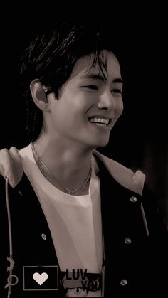 the young man is smiling and wearing a black jacket, white shirt and silver necklace