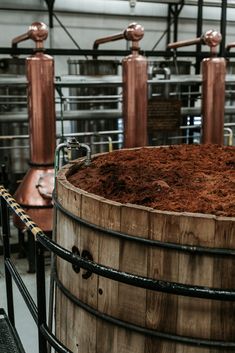 an old wooden barrel with some brown stuff in it and several copper pipes behind it