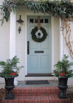 a blue front door with two planters and a wreath on it