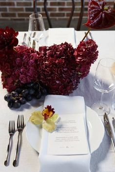 the table is set with white plates, silverware and red flowers in vases